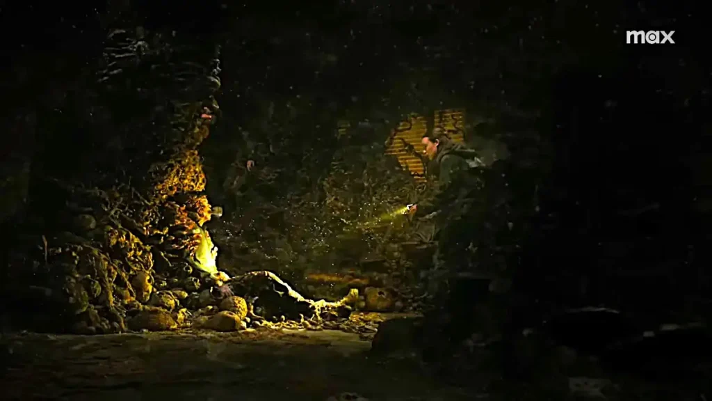 A grotesque infected is trapped in a fungal-covered wall in a dark, damp environment, illustrating the horror of The Last of Us season 2.