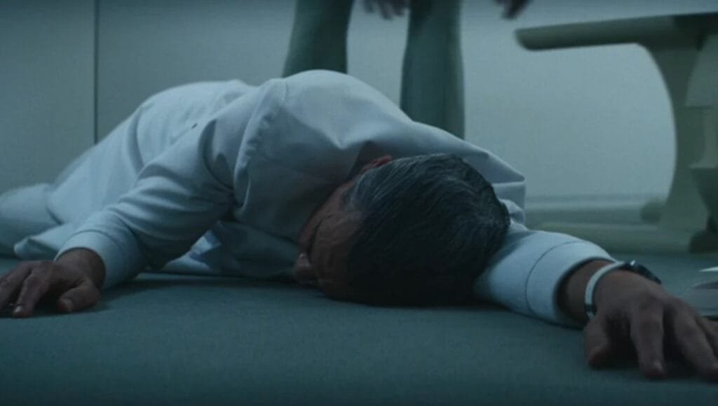 Dr. Mauer lying unconscious on the floor, wearing Lumon's white attire. In the background, someone's silhouette approaches.