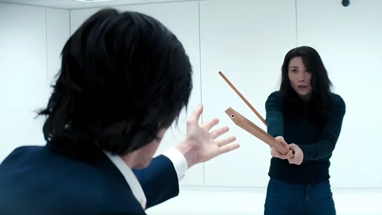 Inside one of Lumon’s stark white rooms, Gemma holds a broken wooden staff in a defensive stance against Mark. The scene suggests a tense moment of recognition or confrontation, where the truth about her identity may be on the verge of revelation. Cold Harbor in Severance