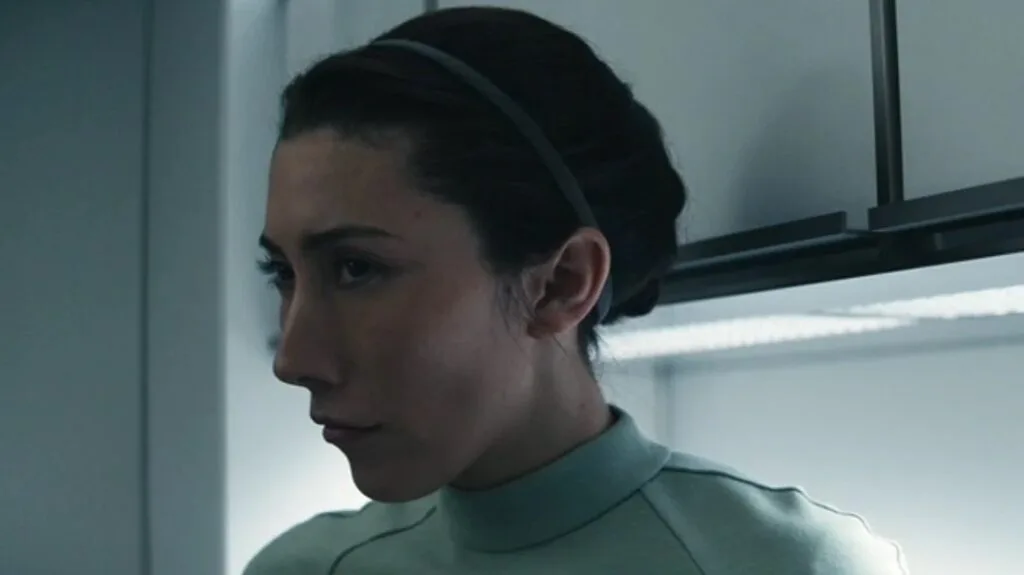 Gemma looking to the side with a serious and determined expression, wearing Lumon's green uniform.