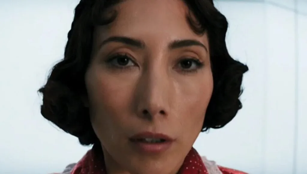 Close-up of a frightened Gemma, wearing red clothes, just as the rupture is activated in the Christmas card room.