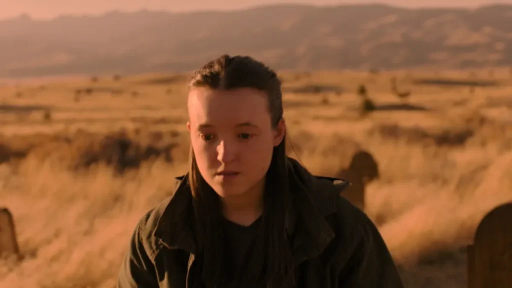 Ellie está em frente a um túmulo, com expressão abatida, durante o pôr do sol em uma cena da 2ª temporada de The Last of Us que representa seu luto por Joel.