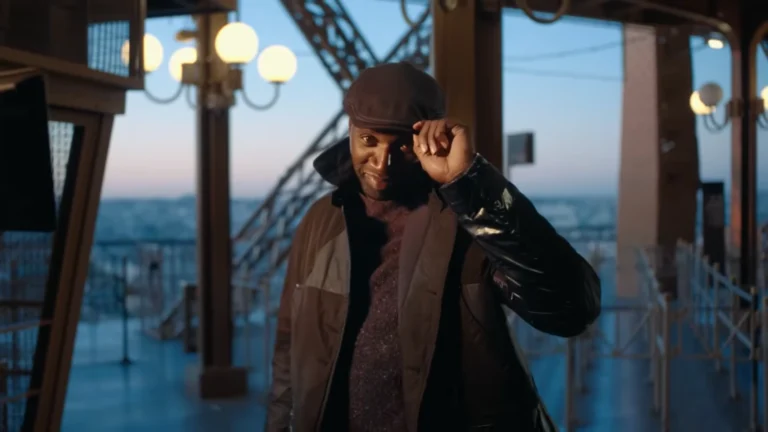 Cena do teaser da Parte 4 de Lupin mostra Omar Sy, como Assane Diop, levantando discretamente o boné no alto da Torre Eiffel ao entardecer.