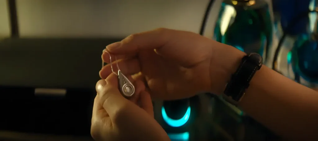 Hands holding the silver necklace that allows reality manipulation in Black Mirror's Bête Noire episode.