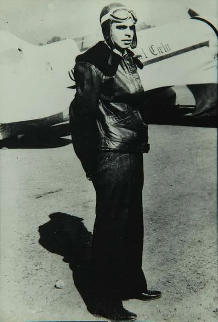 Francisco Sarabia em pé diante de seu avião R-6H 'Conquistador del Cielo', vestindo jaqueta de couro e capacete de voo. Fotografia histórica em preto e branco.