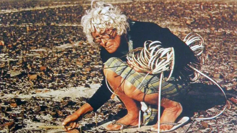 Maria Reiche kneeling in the Nazca desert, using measuring tapes to map the lines traced on the ground.