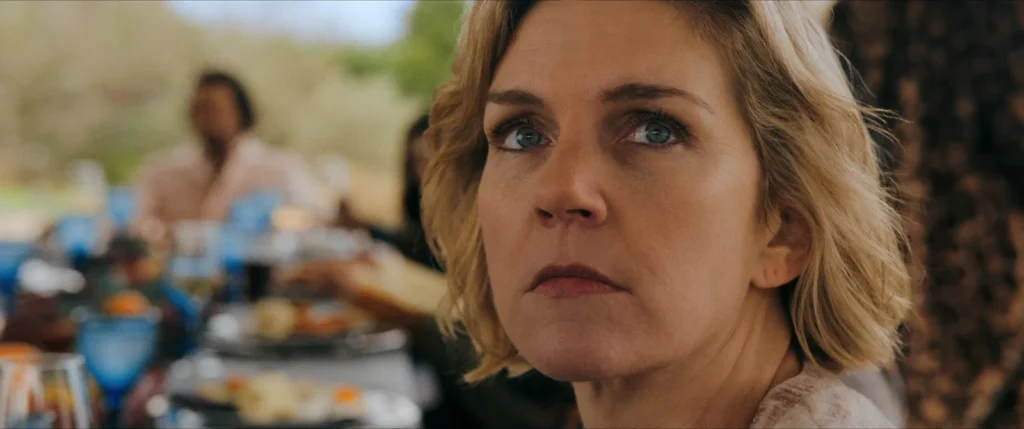 Close-up of Carol during a lunch with the non-infected in the series Pluribus, highlighting tension, surveillance, and the social divide between groups.